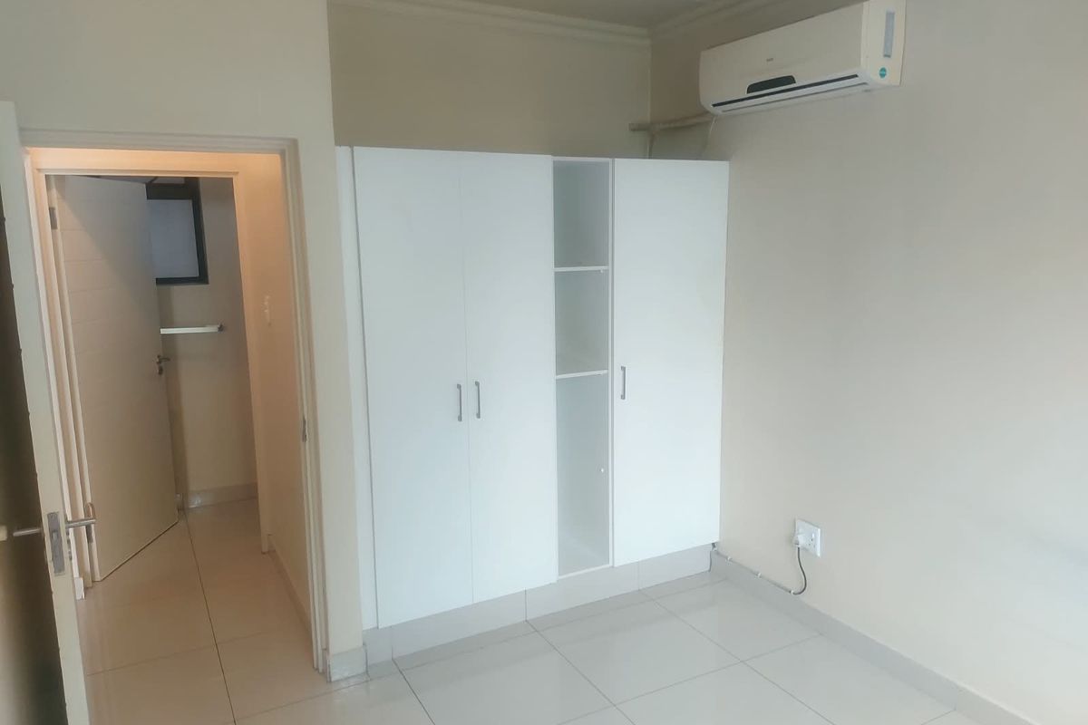 A clean, empty bedroom featuring neutral tiled flooring, a modern built-in wardrobe, and a wall-mounted split-system air conditioning unit.