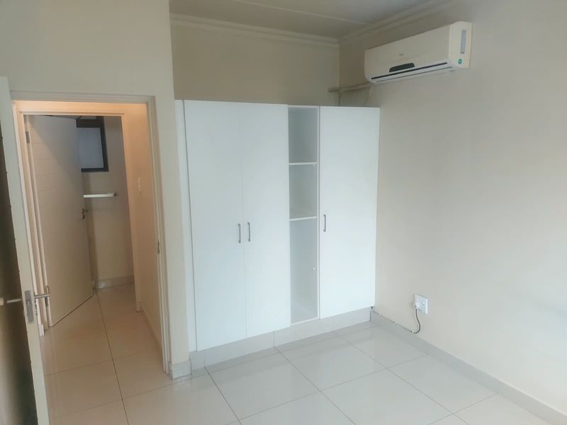 A clean, empty bedroom featuring neutral tiled flooring, a modern built-in wardrobe, and a wall-mounted split-system air conditioning unit.
