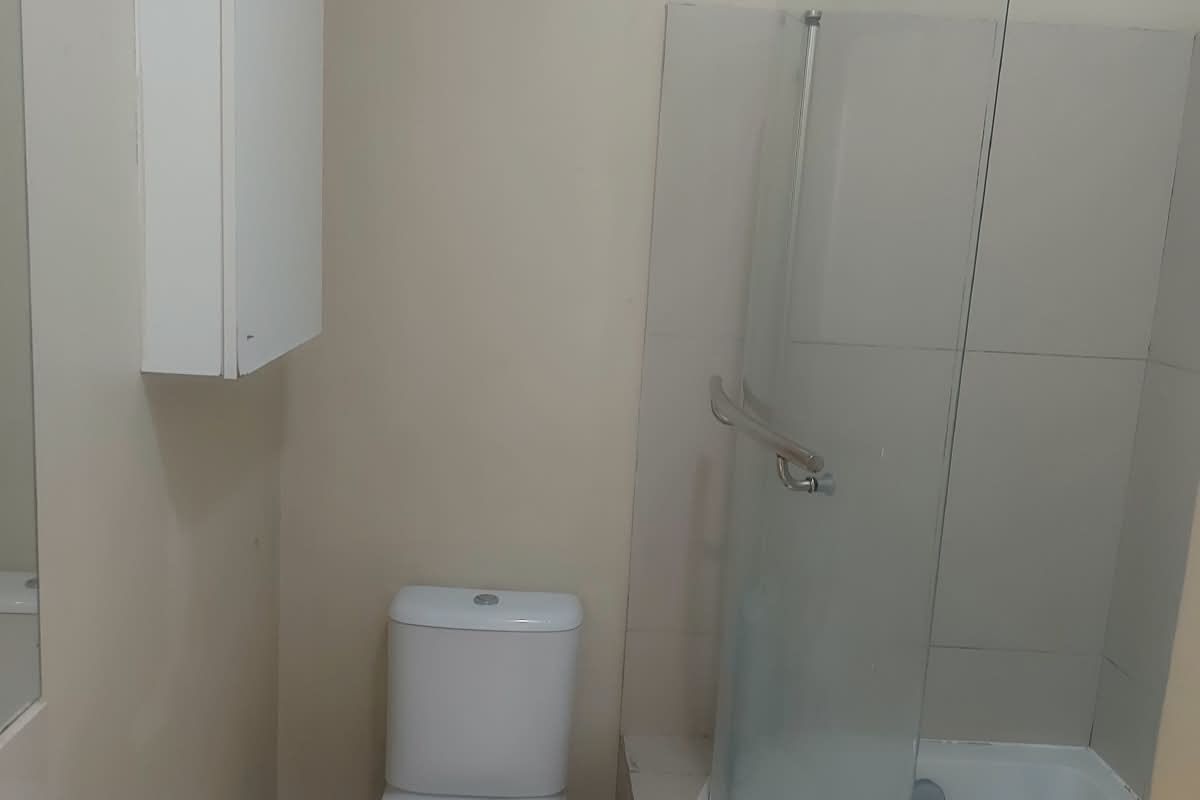 A functional bathroom featuring a pedestal basin, toilet, and a curved glass shower-bath combination with tiled surround.