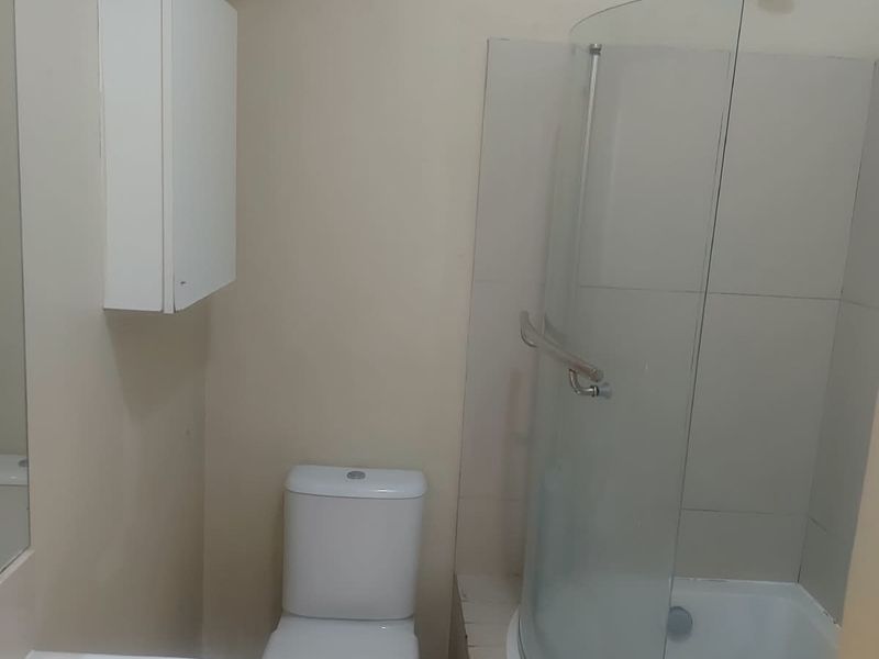 A functional bathroom featuring a pedestal basin, toilet, and a curved glass shower-bath combination with tiled surround.