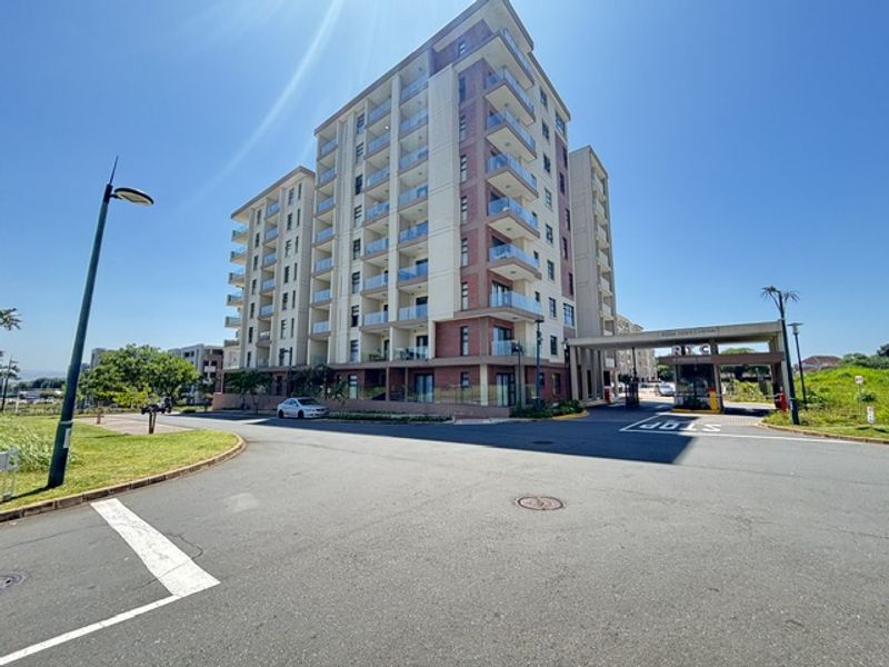 Exterior view of a modern multi-story apartment complex featuring brick cladding, glass balconies, and a secure gated entrance.