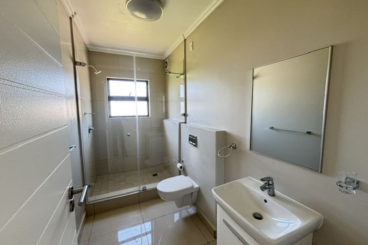 A modern, clean bathroom featuring a wall-mounted toilet, a glass-enclosed shower, and a vanity basin with a wall-mounted mirror.