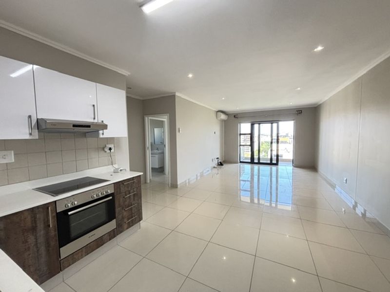 Spacious open-plan living area featuring a modern kitchen with built-in appliances, tiled flooring, and access to a balcony through large sliding glass doors.