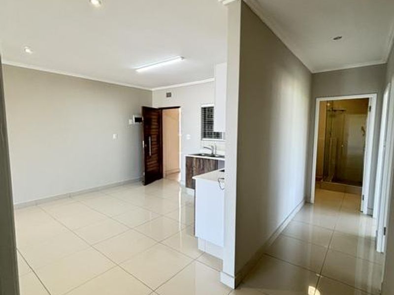 An open-plan living and kitchen area featuring neutral tiled flooring, recessed lighting, and a modern kitchen layout, leading to a separate bathroom area.