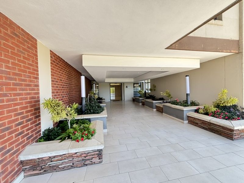 A well-maintained covered entrance area featuring brick wall accents, stone-clad planter boxes, and clean tiled flooring leading to the building access point.