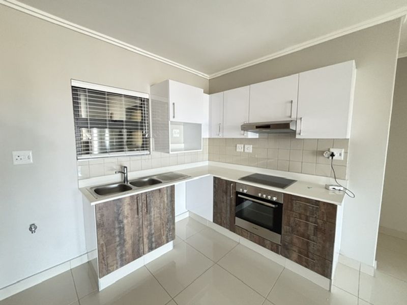 Modern kitchen featuring two-tone cabinetry, stainless steel appliances including a built-in oven and hob, tiled backsplash, and neutral floor tiles.