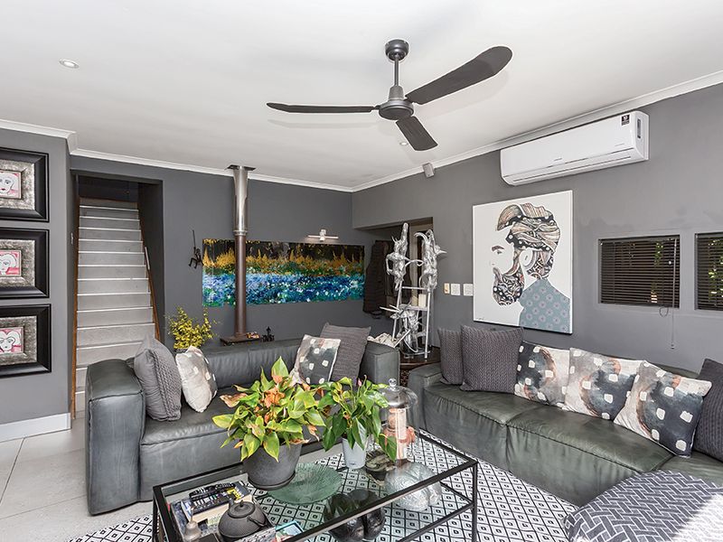 A modern living room featuring a sleek ceiling fan, split-system air conditioning, and a contemporary freestanding fireplace, with stairs leading to an upper level.