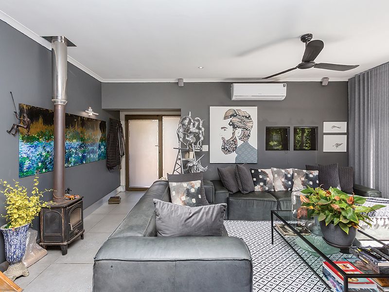 A modern living room featuring a freestanding fireplace, split-system air conditioning, ceiling fan, and tiled flooring with access to an outdoor area.