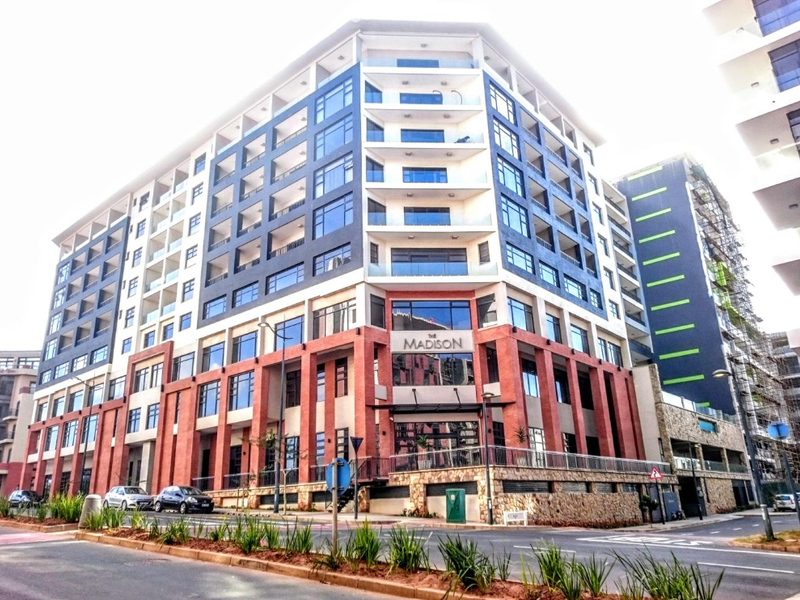 A modern multi-story apartment building featuring a prominent brick and glass facade with integrated balconies and street-level access.