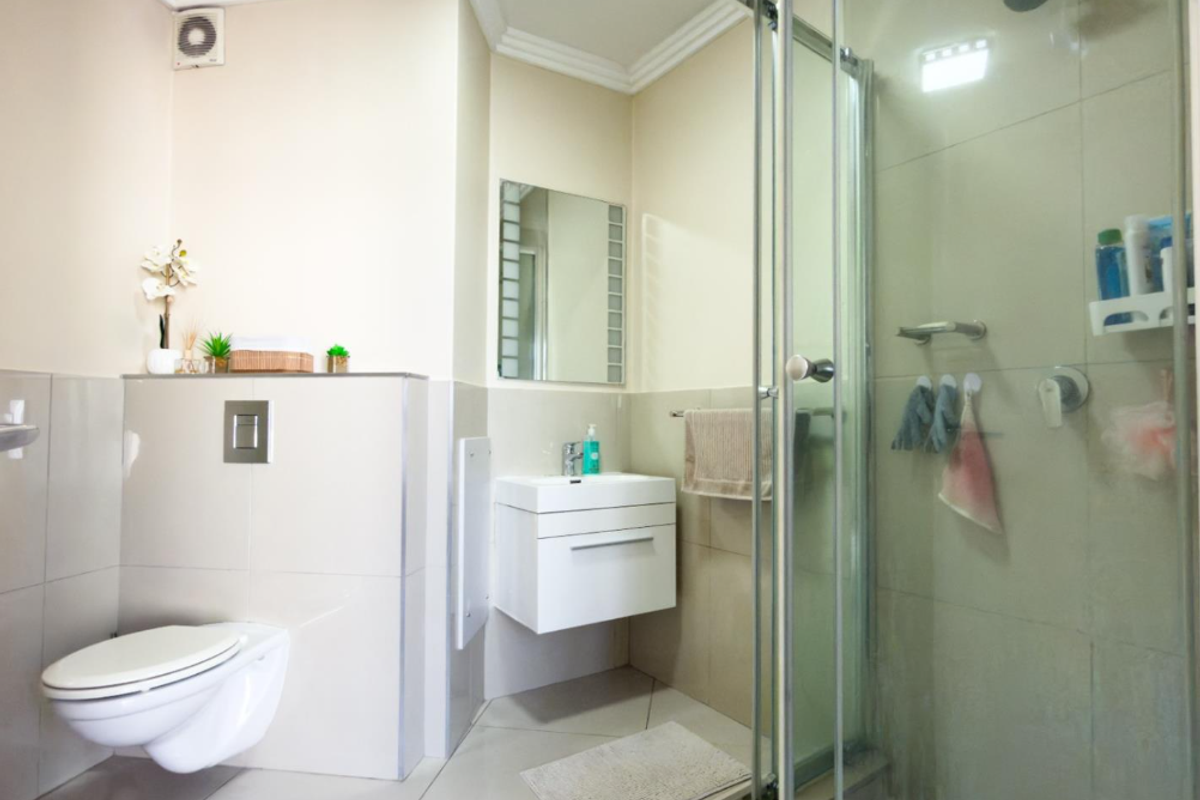A modern bathroom featuring a wall-mounted toilet, floating vanity, and a glass-enclosed shower with neutral tiling throughout.
