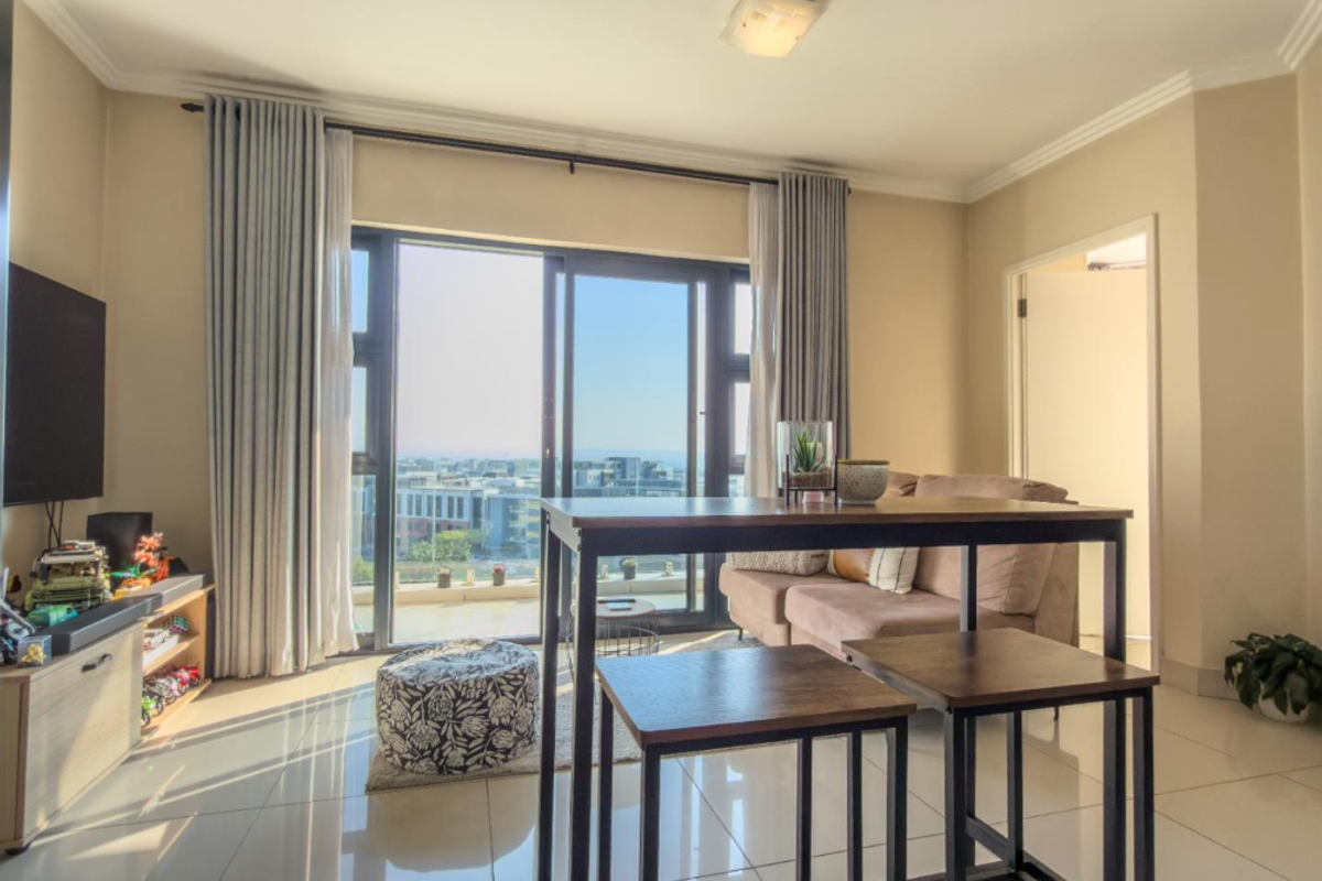 A bright living room featuring large sliding glass doors that open to a balcony, polished tiled floors, and neutral wall finishes.