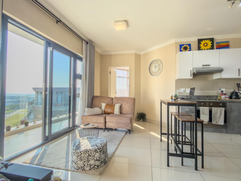 Bright open-plan living area featuring modern kitchen cabinetry, granite countertops, and large sliding glass doors leading to a balcony with natural light.