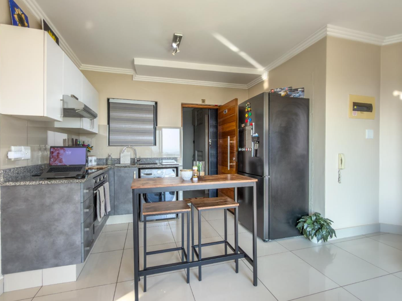 Modern kitchen featuring granite countertops, ample built-in cabinetry, stainless steel sink, and tiled flooring, offering a functional and contemporary cooking space.