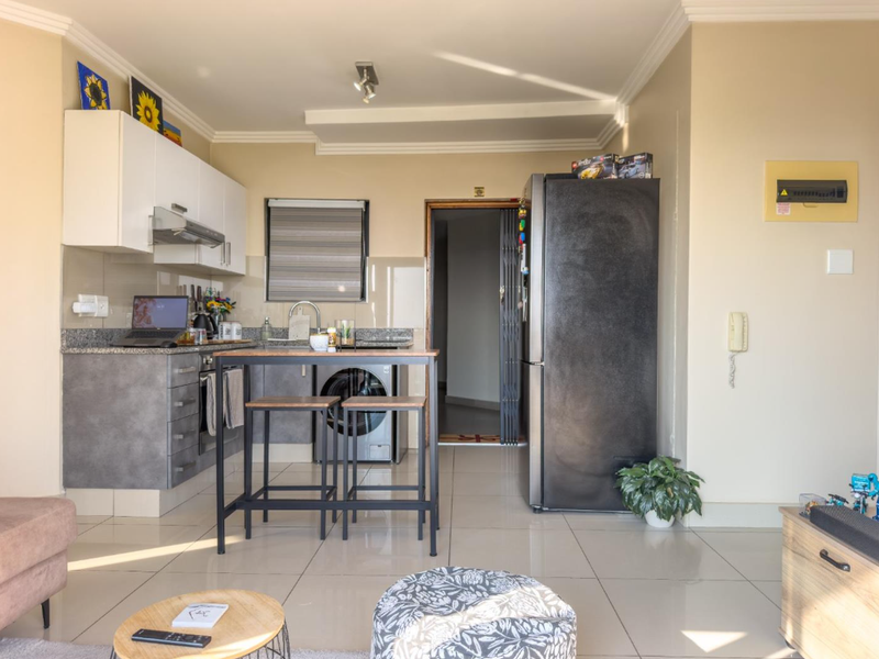 Open-plan kitchen area featuring modern grey cabinetry, granite countertops, tiled flooring, and integrated appliance space, seamlessly connecting to the living area.