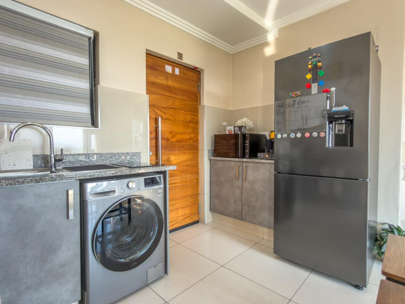 A modern, well-maintained laundry area featuring granite countertops, built-in cabinetry, tiled flooring, and a sleek chrome mixer tap.