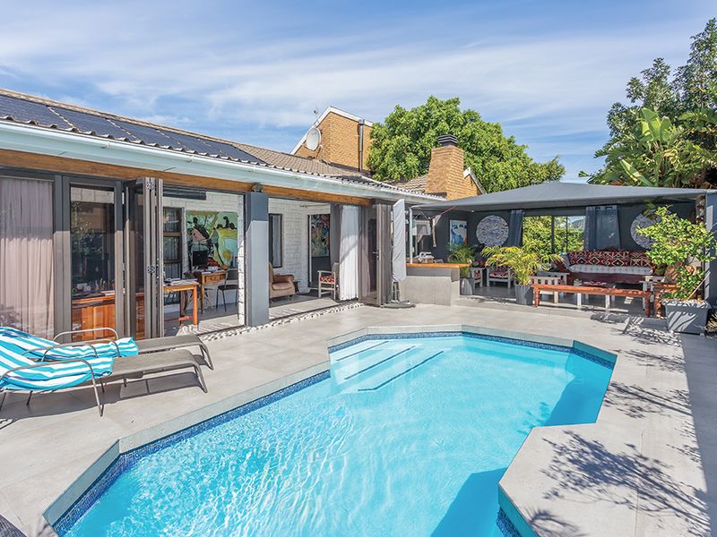 A well-maintained outdoor pool area featuring a tiled deck, covered patio space, and seamless indoor-outdoor flow through large bi-fold doors.
