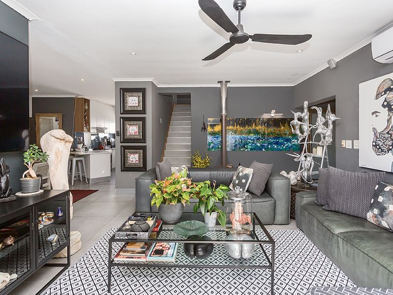 Spacious open-plan living area featuring tiled floors, a modern ceiling fan, split-system air conditioning, and a staircase leading to the upper level.