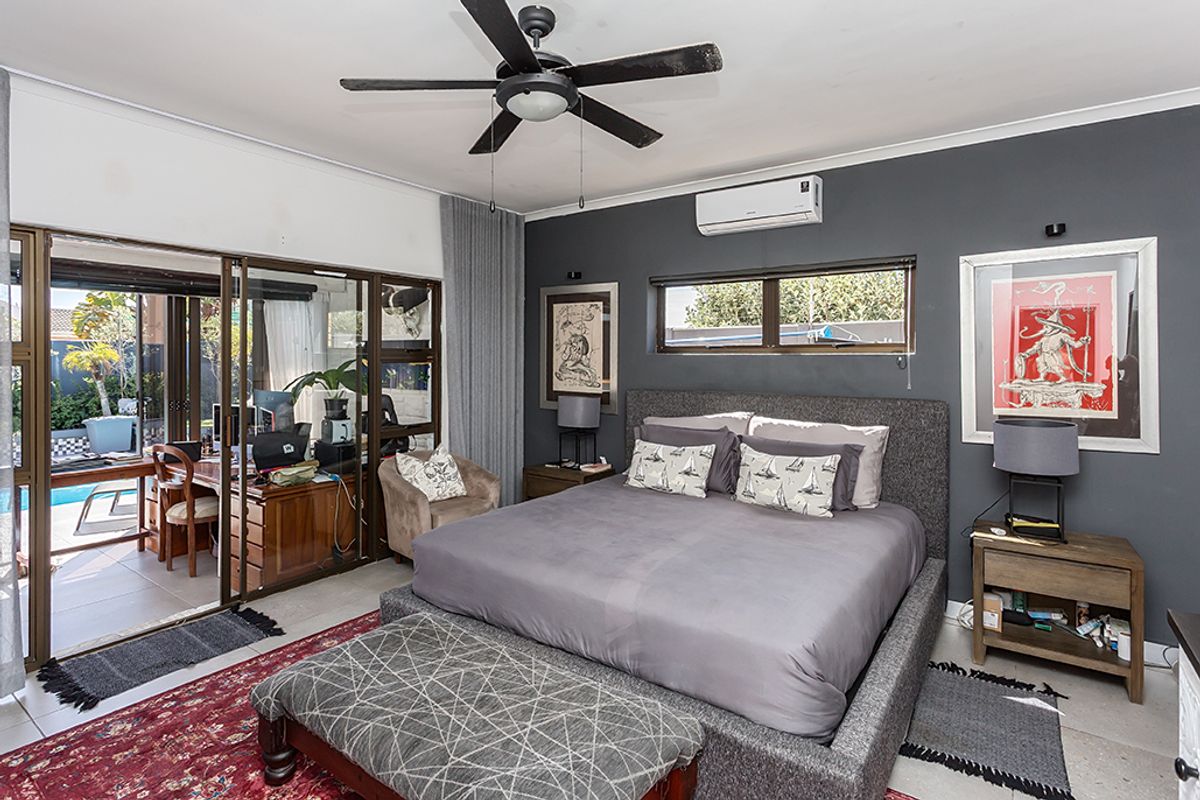 Spacious bedroom featuring a ceiling fan, split-system air conditioning, and large sliding glass doors providing direct access to the outdoor pool area.