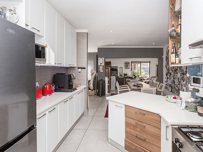 Modern open-plan kitchen featuring sleek white cabinetry, a functional island with wood-grain accents, gas hob, and seamless flow into the adjacent dining area.