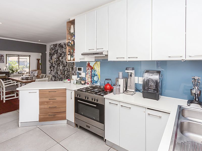 Modern open-plan kitchen featuring white cabinetry, gas stove with extractor, glass splashback, and double stainless steel sink, flowing into the adjacent dining area.