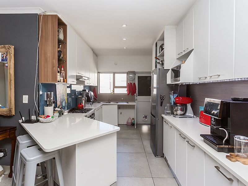 A functional galley-style kitchen featuring white cabinetry, stone countertops, a gas hob, and integrated appliances with tiled flooring and recessed lighting.
