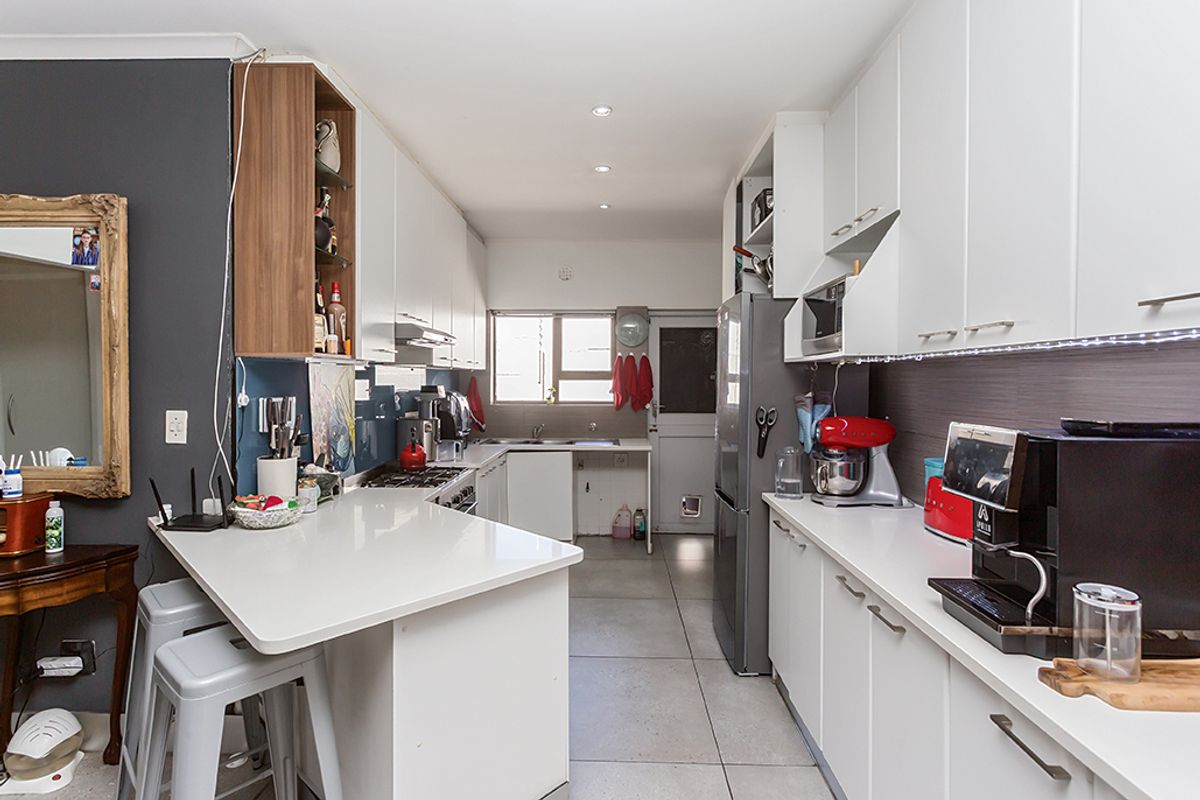 A functional galley-style kitchen featuring white cabinetry, stone countertops, a gas hob, and integrated appliances with tiled flooring and recessed lighting.