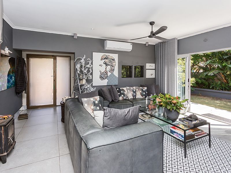 Modern living room featuring a cast iron fireplace, split system air conditioning, ceiling fan, and large sliding glass doors opening to the garden.
