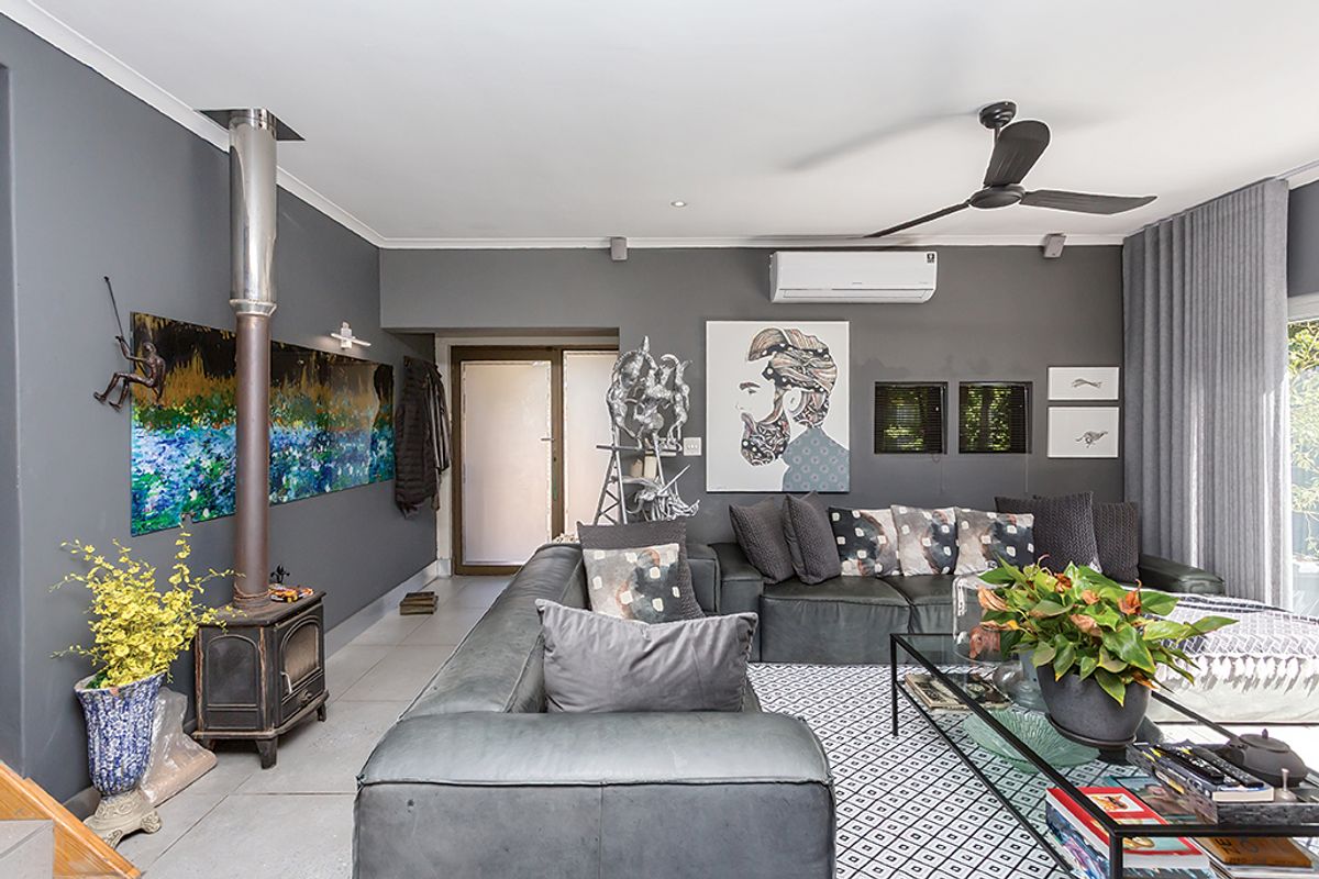 A modern living room featuring a freestanding fireplace, split-system air conditioning, ceiling fan, and tiled flooring with access to an outdoor area.