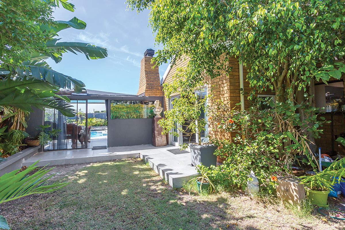 Rear view of the property featuring a brick facade, a tiled patio area, and a prominent brick chimney, overlooking a garden space.