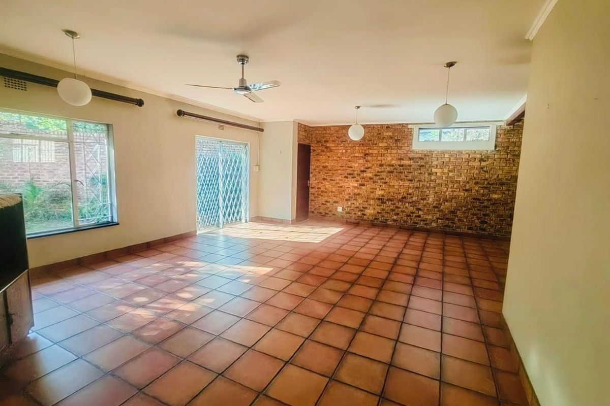 Spacious living area featuring terracotta floor tiles, an exposed brick feature wall, ceiling fan, and sliding glass doors leading to the exterior.