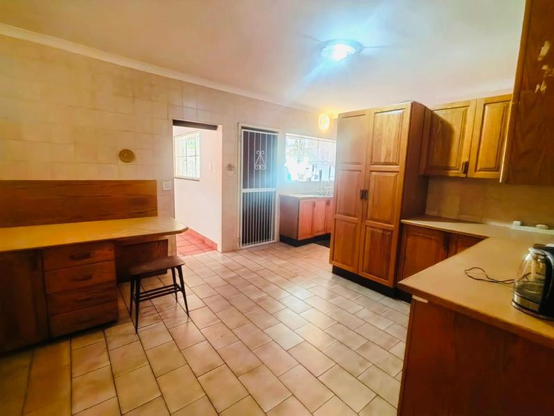 A functional kitchen featuring wooden cabinetry, tiled flooring, and a built-in desk area, offering a dated but practical layout with potential for modernization.