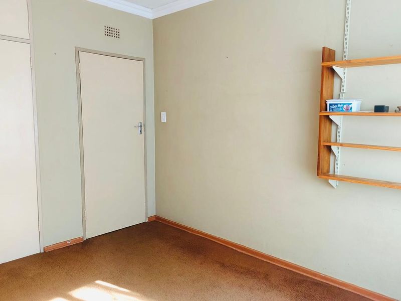 A vacant bedroom featuring built-in cupboard storage, wall-mounted shelving, and carpeted flooring, presenting a blank canvas for potential updates.