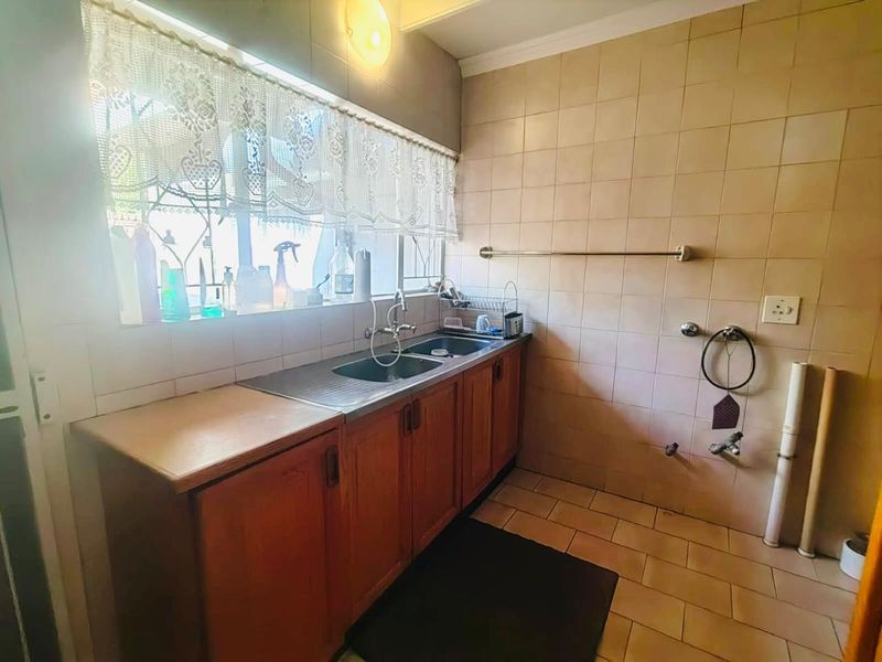 A functional laundry room featuring built-in wooden cabinetry, a double stainless steel sink, and dedicated plumbing connections for laundry appliances.