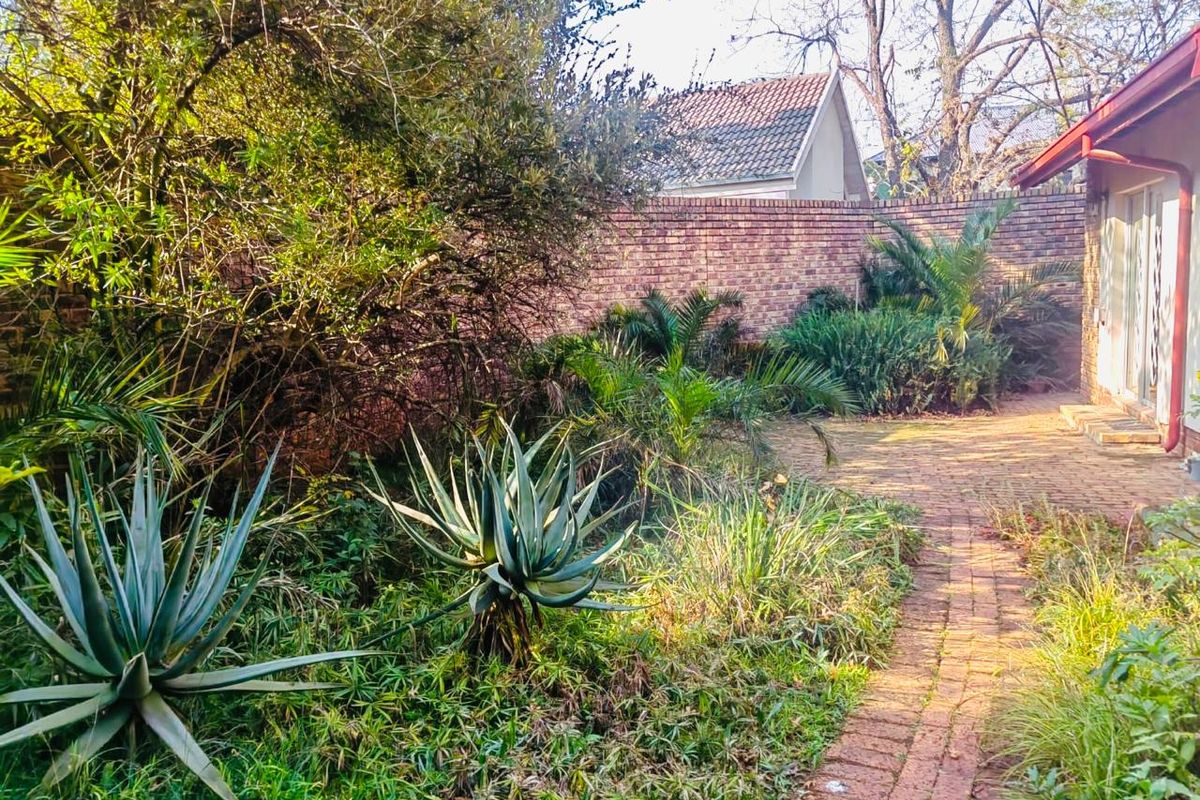 A private rear garden featuring a brick paved pathway, established landscaping, and a high brick boundary wall for added privacy.