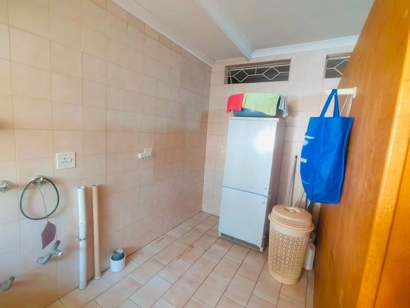 A functional laundry area featuring tiled walls and flooring with dedicated plumbing connections and high-level security windows.