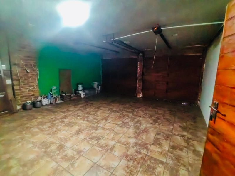 A spacious, empty garage featuring tiled flooring, exposed brick accents, and a ceiling-mounted door motor, offering potential for storage or workshop use.