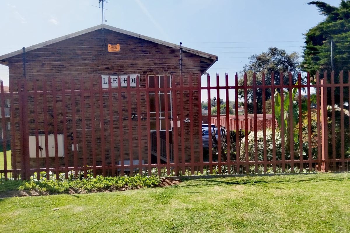 Rear view of the face-brick apartment building featuring secure steel palisade fencing and established garden area.