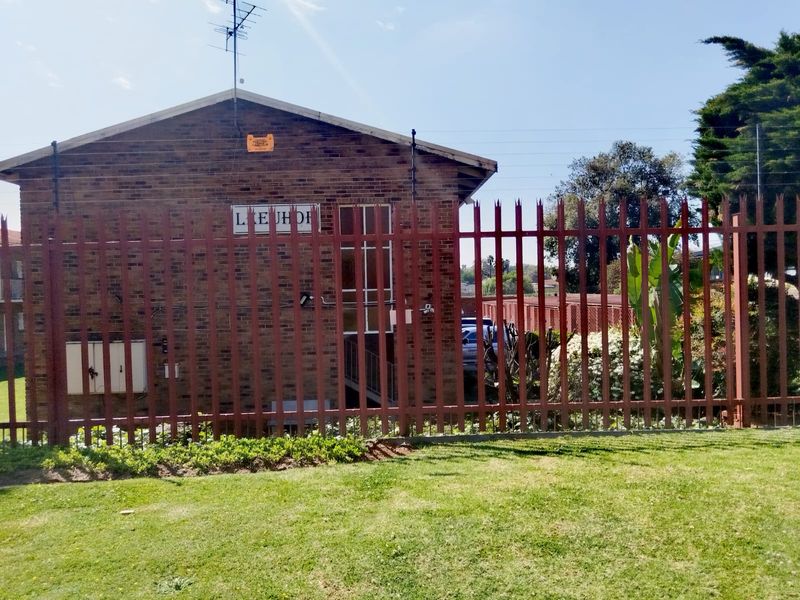 Rear view of the face-brick apartment building featuring secure steel palisade fencing and established garden area.