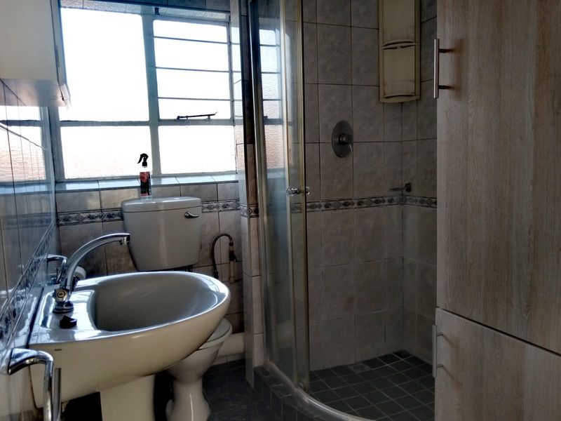 A functional bathroom featuring a pedestal basin, a shower enclosure with tiled walls, and built-in cabinetry, offering a practical layout with natural light.