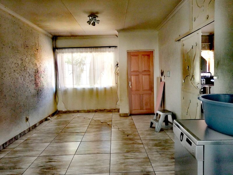 An empty living area featuring tiled flooring and a timber door, requiring significant cosmetic renovation and wall repairs to restore the space.