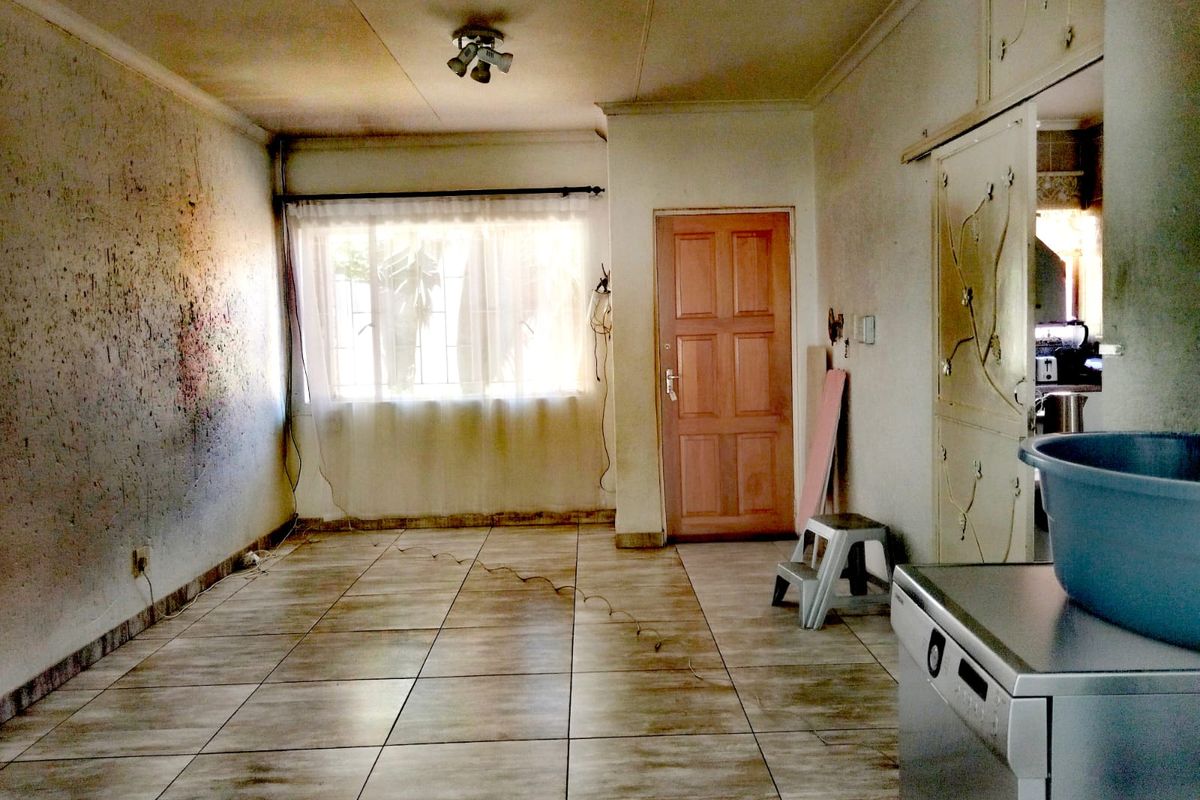 An empty living area featuring tiled flooring and a timber door, requiring significant cosmetic renovation and wall repairs to restore the space.