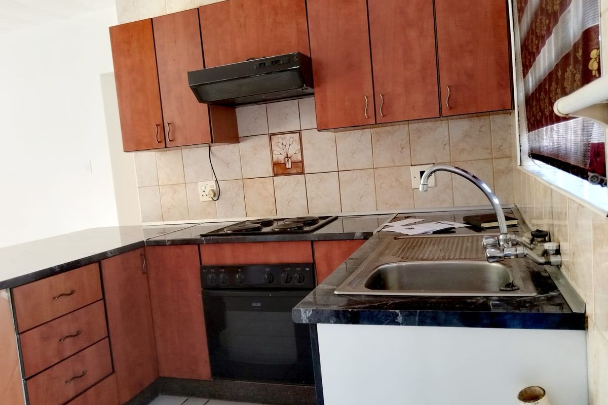 A functional kitchen featuring wooden cabinetry, dark laminate countertops, a built-in oven with hob, and tiled splashbacks.