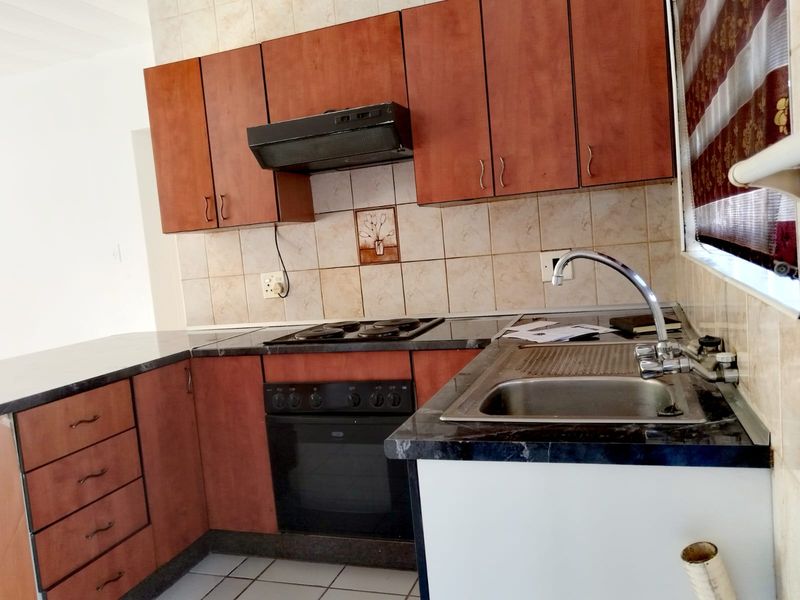 A functional kitchen featuring wooden cabinetry, dark laminate countertops, a built-in oven with hob, and tiled splashbacks.