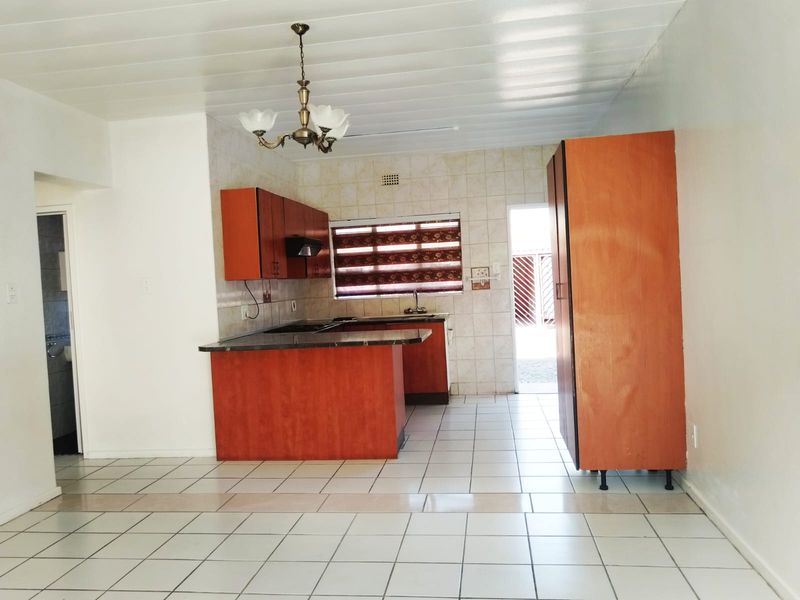 A functional kitchen featuring built-in cabinetry, tiled flooring, and a tiled backsplash, offering a practical layout with direct access to an exterior area.