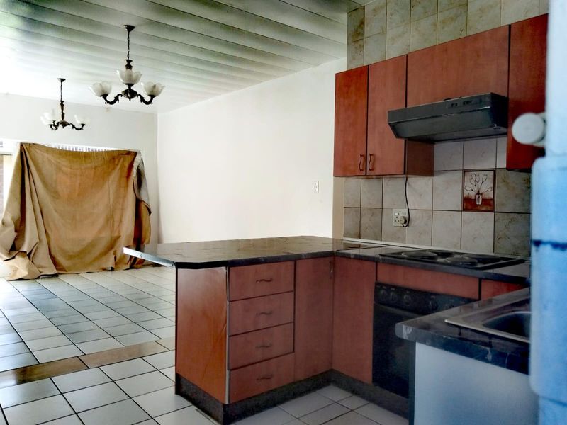 Open-plan kitchen and living area featuring tiled flooring, built-in cabinetry with integrated oven and hob, and classic ceiling light fixtures.