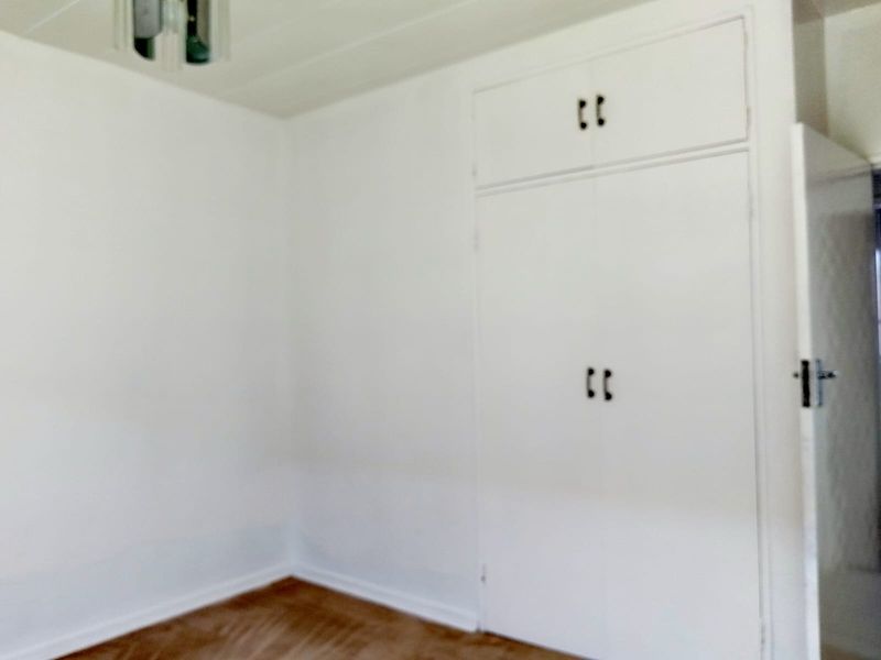 A vacant bedroom featuring white walls, wooden flooring, and built-in cupboards with overhead storage compartments.