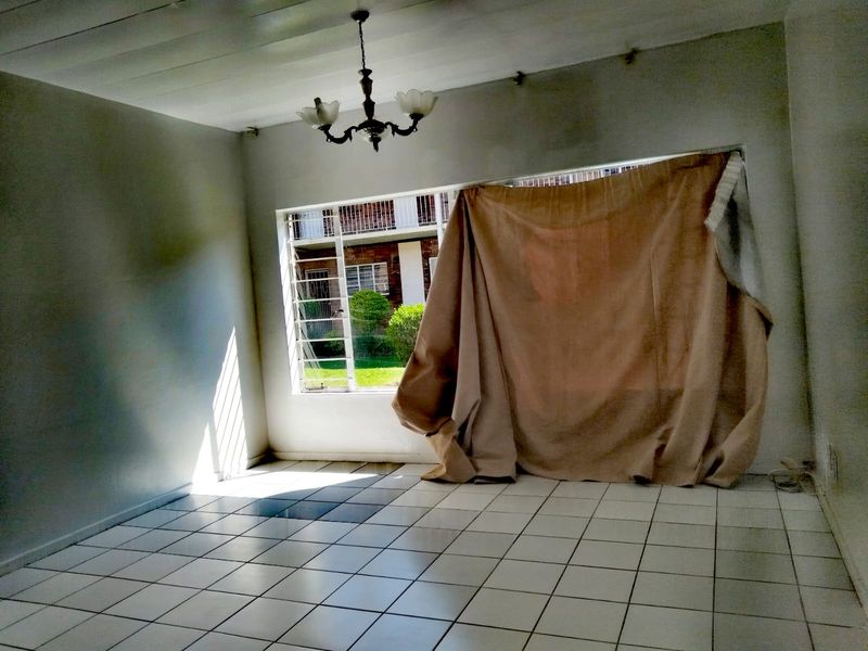 An empty living room featuring tiled flooring, a ceiling light fixture, and a large window with security bars, offering a blank canvas for renovation.
