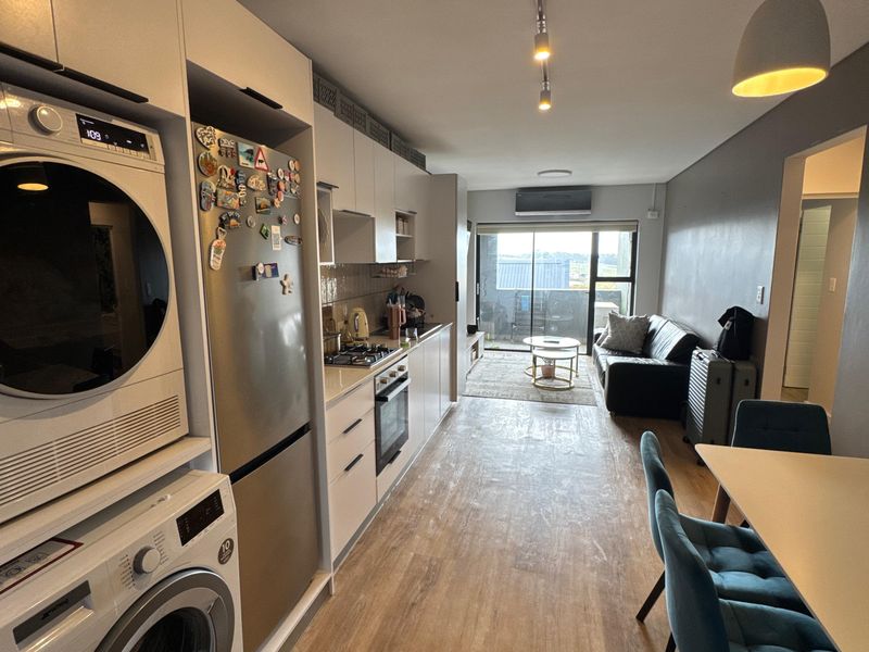 Modern open-plan living area featuring a sleek kitchen with built-in appliances, laundry facilities, and direct access to a balcony through sliding glass doors.