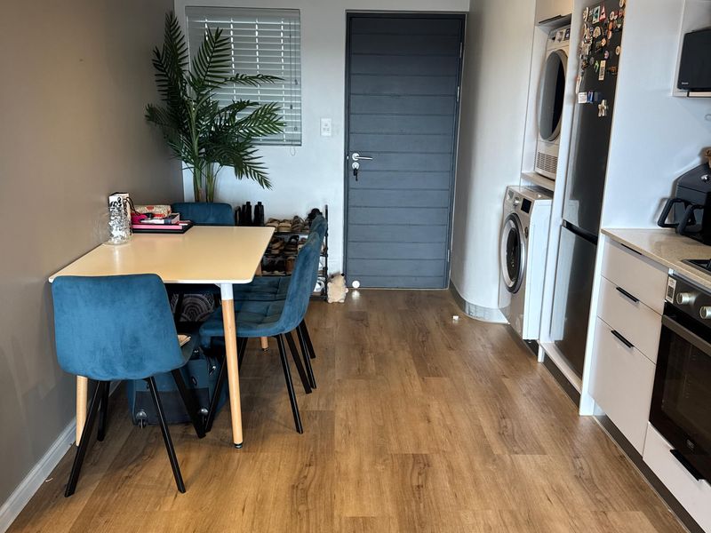 Modern open-plan apartment living area featuring laminate flooring, integrated kitchen cabinetry with built-in oven, and a dedicated laundry nook.