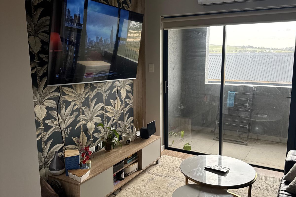 A well-maintained living room featuring a decorative wallpaper accent wall, split-system air conditioning, and direct access to a private balcony through sliding glass doors.